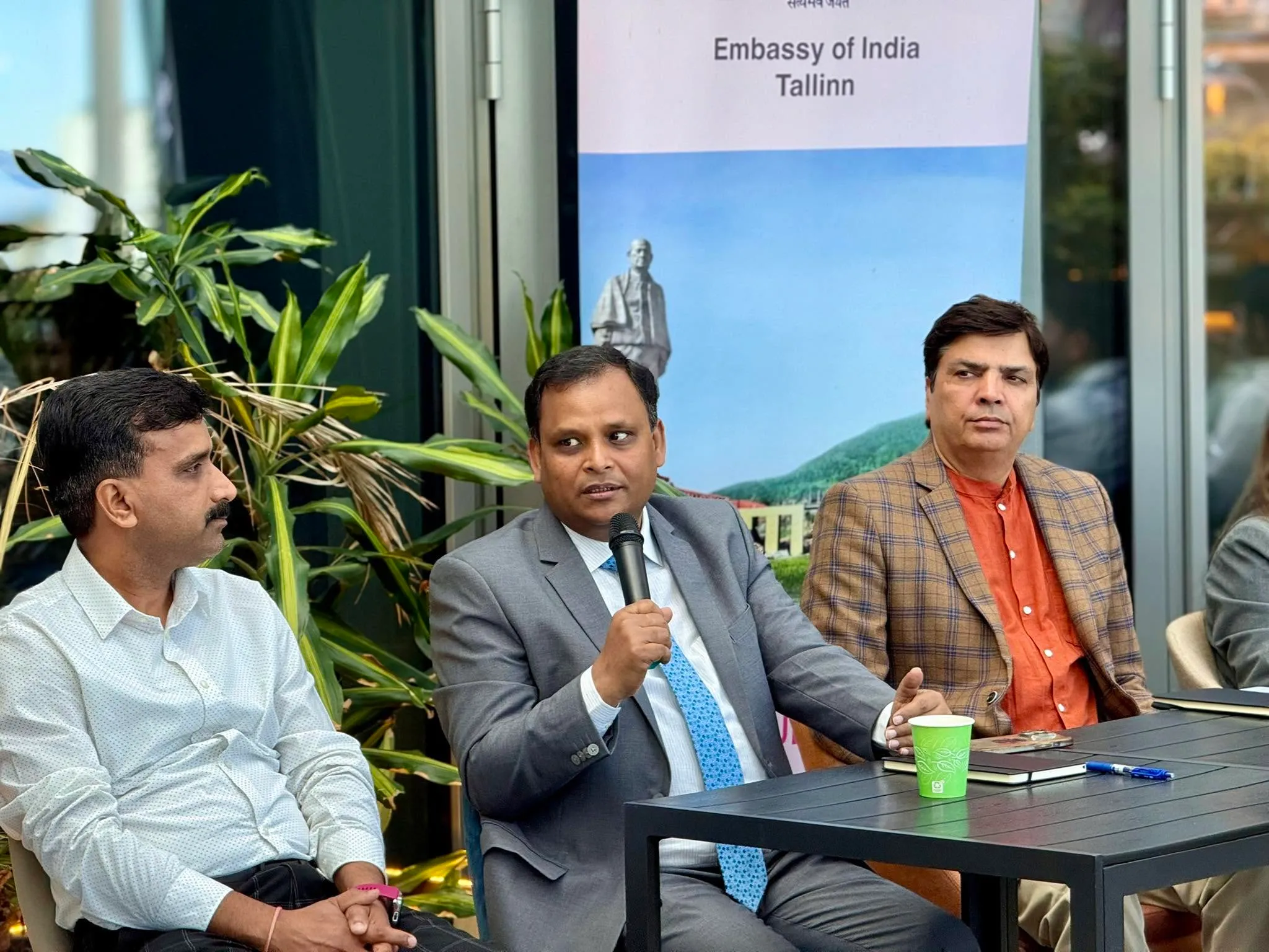 Tema Ekstsellents suursaadik Ashish Sinha räägib mikrofoni, istudes laua taga kahe külalise vahel, taustal India saatkonna plakat