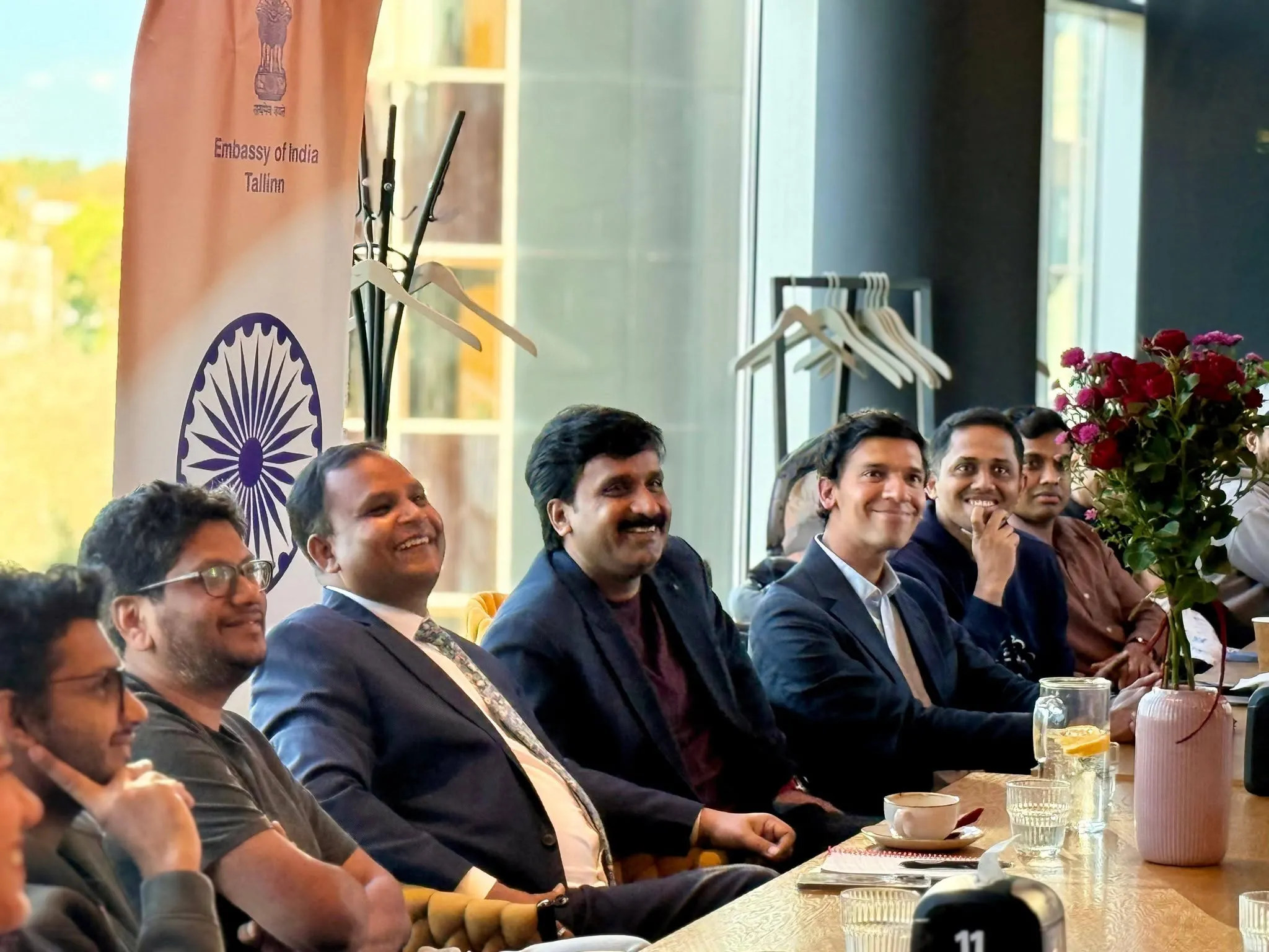 Suursaadik ja külalised naeratamas pika laua taga Tartus, taustal India saatkonna plakat